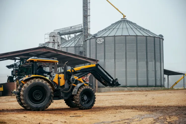 Yellow Valtra loader working beside grain silos