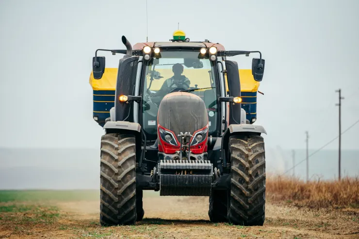 Red Valtra tractor spreading fertiliser in a field